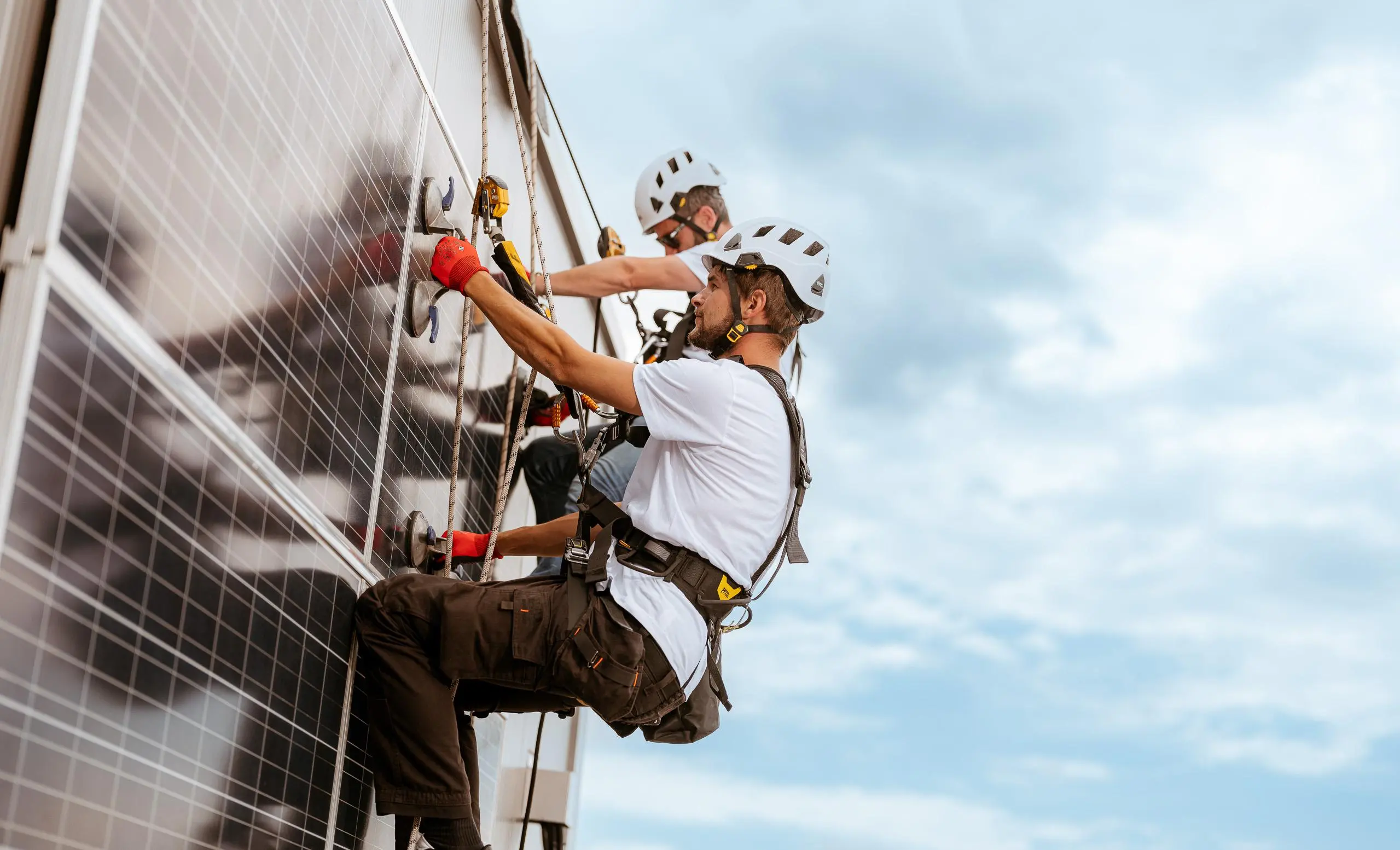 Zwei Arbeiter installieren PV-Anlage an einer Fassade eines Gebäudes